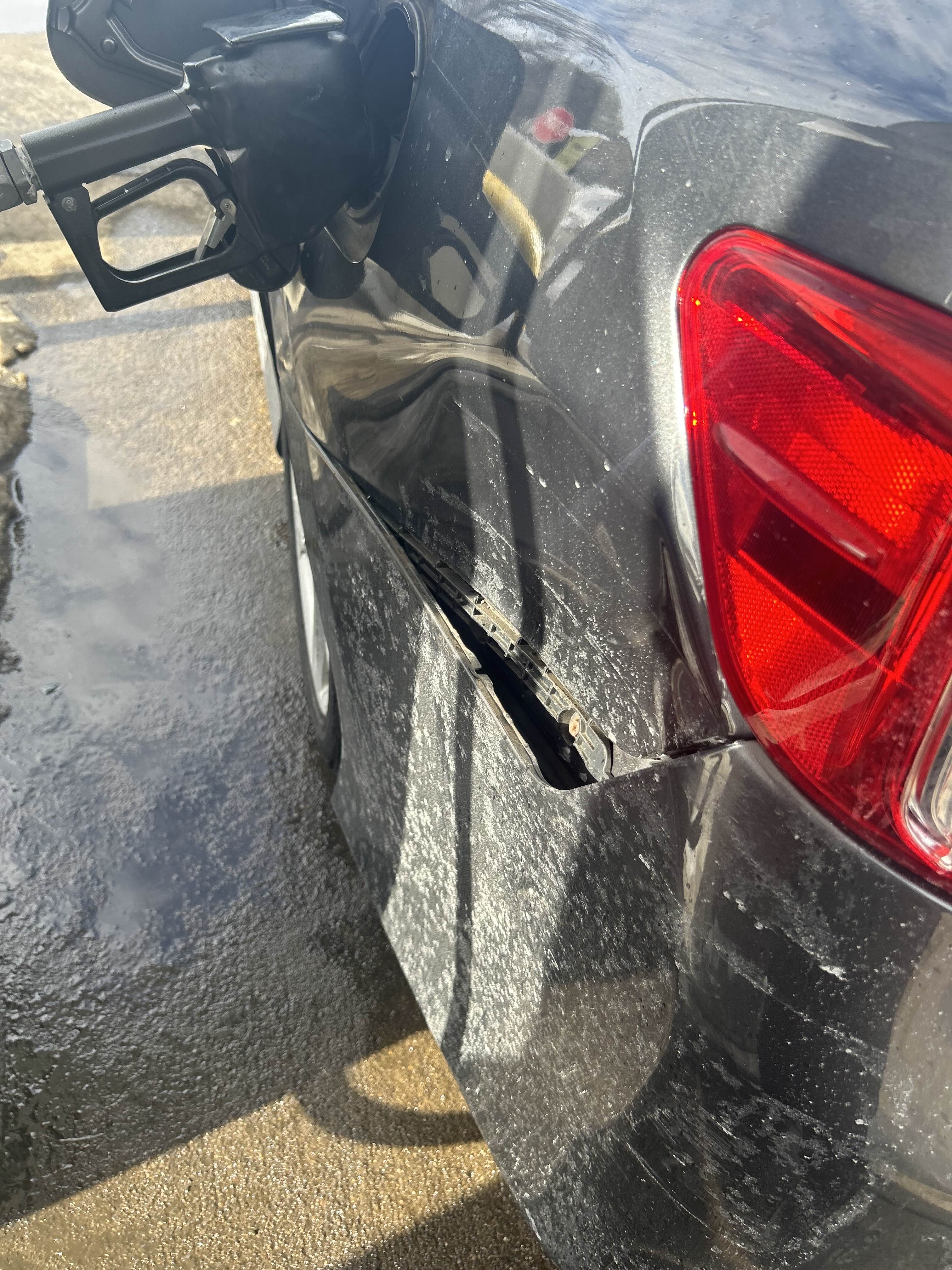 Image of a grey car from the back driver's side. The panel connecting the rear bumper to the side panel of the car are dented in by several inches. The inside of the car can be seen and there are multiple scratches.